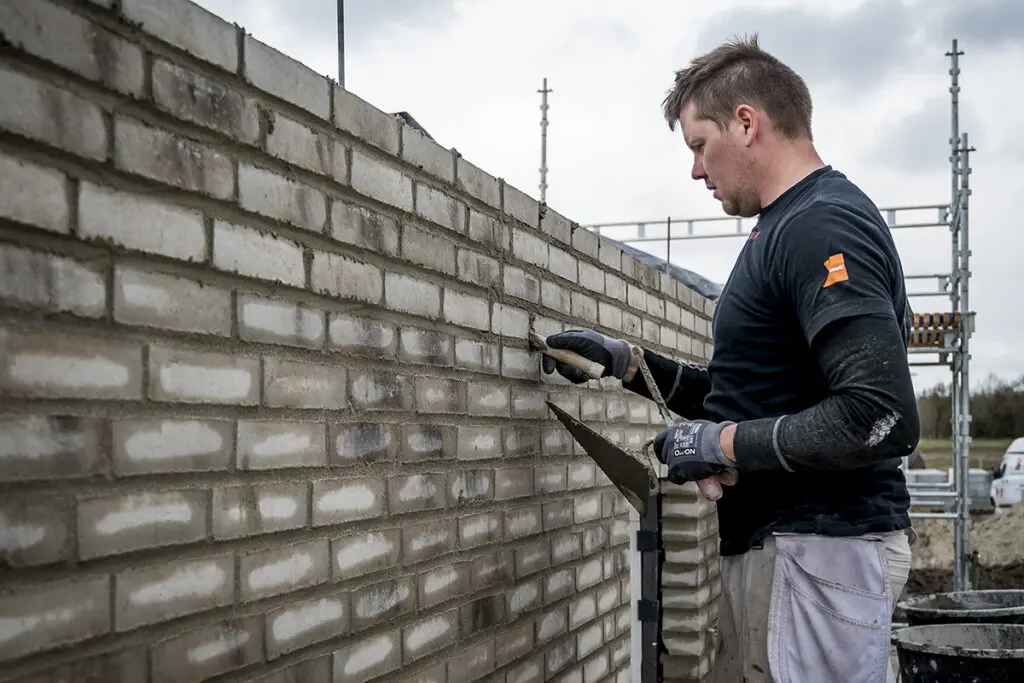 Murer fra Preben Poulsen udfører præcisionsarbejde med fuge og mursten under renovering af murværk.
