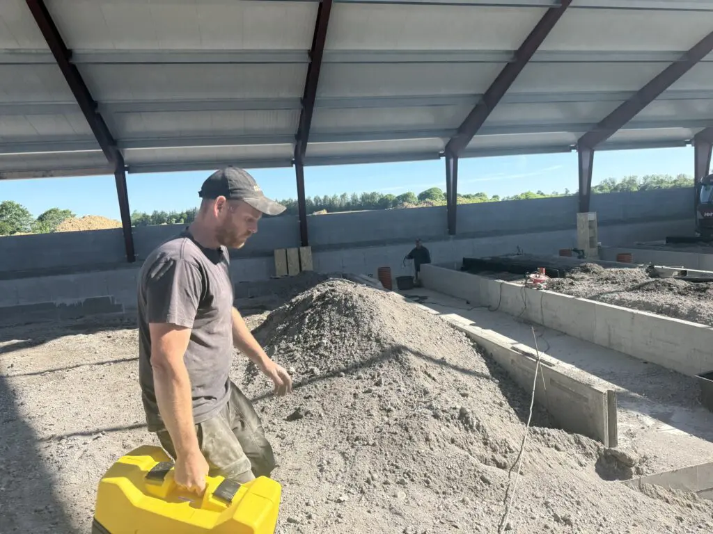 Medarbejder fra Preben Poulsen udfører betonarbejde og jordarbejde i en ny staldbygning.